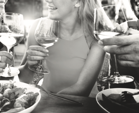 Close up photo of a woman and two friends seated together and sipping wine with their food