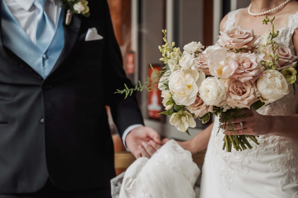 Closeup shot of a bride holding hands with the groom, with a rose bouquet in her other hand